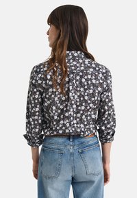 Camicia nera a fiori con fiori bianchi, design con bottoni e maniche arrotolate, abbinata a jeans in denim azzurro chiaro, con tasche posteriori.