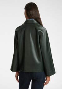 Giacca di pelle verde scuro con vestibilità ampia, maniche larghe e colletto classico, caratterizzata da una texture liscia e lucida.