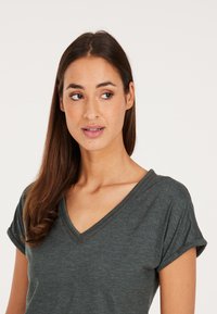 T-shirt grigio scuro a V con maniche arrotolate, realizzato in tessuto morbido. Dettaglio di cucitura evidente lungo il colletto. Vestibilità casual.