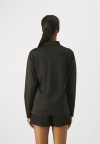 Svart langermet skjorte laget av glatt stoff, med krage og avslappet passform, paret med svarte shorts. Teksturert overflate uten mønster.