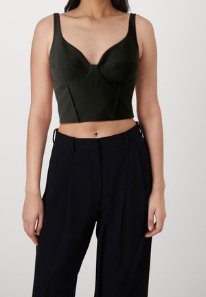 Kobieta ubrana w czarny dopasowany crop top z szerokimi ramiączkami oraz czarne, luźne spodnie z wysokim stanem na jednolitym tle.