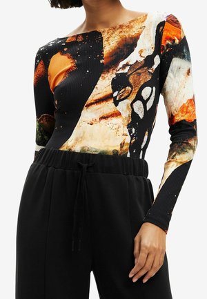 Femme portant un haut ajusté à manches longues avec des motifs abstraits orange, noir, blanc et beige, assorti à un pantalon noir à cordon de serrage.