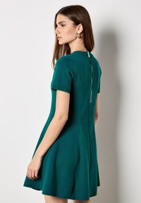 Abito teal attillato a manica corta con gonna svasata e zip sul retro. Tessuto testurizzato con una finitura liscia.