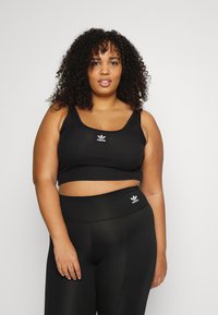 Top corto nero a costine con spalline larghe, caratterizzato da un piccolo logo bianco Adidas. Leggings neri a vita alta, anch'essi con un logo bianco sulla cintura.