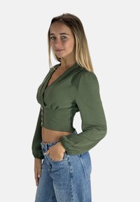 Olivgrüne, kurz geschnittene Bluse mit V-Ausschnitt, Knopfdetails und langen Puffärmeln, kombiniert mit hoch taillierten blauen Denim-Jeans.