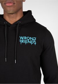 Sudadera negra con cordones, con un logotipo turquesa "WRONG FRIENDS" impreso en el pecho. Tela suave, ajuste regular.