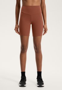 Visoko pasne, oprijete kratke hlače za kolesarjenje v rdeče rjavi barvi, narejene iz elastičnega materiala. Imajo gladko, brezšivno zasnovo in dolžino do sredine stegna.