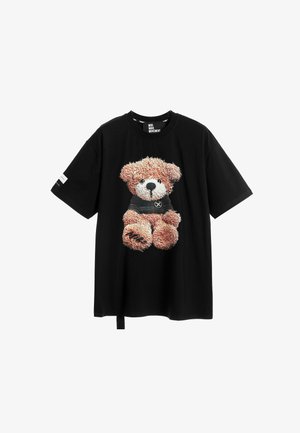 Camiseta de algodón negra con un gráfico de un oso de peluche en marrón y crema, que lleva puesta una camiseta negra. Corte holgado con un detalle de etiqueta lateral.