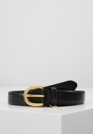Zwarte leren riem met een glanzende gouden ovale gesp en een klein gouden hangertje, opgerold op een witte ondergrond tegen een effen lichte achtergrond.