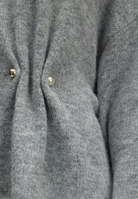 Grijs gebreide trui stof met textuurdetails, met vooraan twee knopen, één van goud en één van parel.