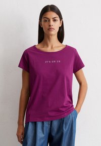 Korte mouwen, ronde hals paarse t-shirt met de tekst "IT'S ON US" in het wit. Gemaakt van zachte katoen, met een ontspannen pasvorm en een soepele textuur.