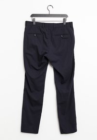 Námořnické modré kalhoty zavěšené na černém ramínku, které mají dvě zadní kapsy s knoflíky a rovný střih. Hladký textura látky.