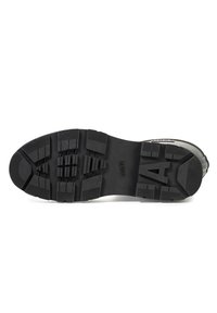 Semelle de chaussure en caoutchouc noir avec des profondeurs de crampons et une surface texturée. Présente un "A" proéminent au centre et des motifs de grip distincts pour l'adhérence.