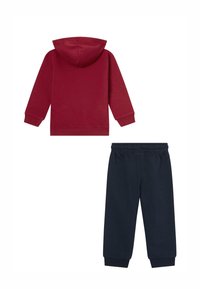 Czerwona bluza z kapturem i długimi rękawami, w połączeniu z ciemnoniebieskimi dresami z elastycznym paskiem i ściągaczami przy mankietach.