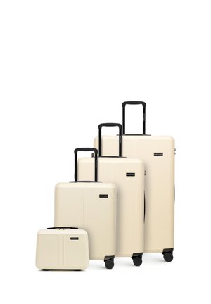 Quatre valises rigides beiges avec poignées et roulettes noires, disposées par taille de la plus petite à la plus grande sur fond blanc.