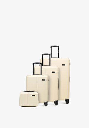 Čtyři béžové tvrdé kufry s černými držadly a kolečky, uspořádané podle velikosti od nejmenšího po největší na bílém pozadí.