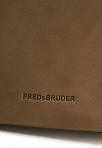 Borsa in pelle marrone con una texture liscia e logo impresso "FREDsBRUDER" in basso, che evidenzia un design minimalista.