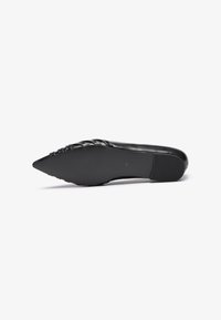 Zapato negro de punta afilada con parte superior de cuero suave, detalle de acento trenzado, suela de goma y tacón plano. Diseño minimalista.