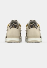 Μπεζ αθλητικά παπούτσια με λεπτομέρειες από δέρμα φιδιού στη φτέρνα, χρυσά μεταλλικά στοιχεία και λευκή μεσαία σόλα. Ομαλή υφή με στιβαρό σχεδιασμό.