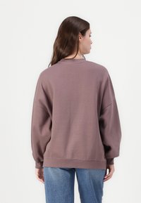 Preveliki dukserica u prigušenoj mauve boji, s okruglim izrezom i dugim, voluminoznim rukavima. Mekani materijal s rebrastim manžetama i rubom.