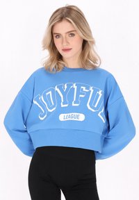 Kék, rövidított pulóver fehér "JOYFUL" felirattal és alatta "LEAGUE" felirattal. Lazán illeszkedő fazon, bordás textúrával az alján.