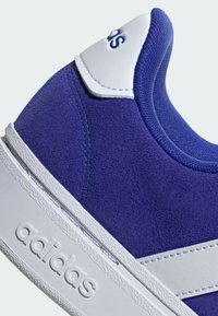 Sneaker viola in suede con dettagli in pelle bianca e una suola in gomma bianca texturizzata. Presenta un logo sulla linguetta e un design a strisce sui lati.