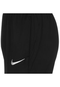 Pantaloni shorts sportivi neri con vita elastica e tasche laterali. Presentano un logo Nike argentato sul lato sinistro. Texture liscia.