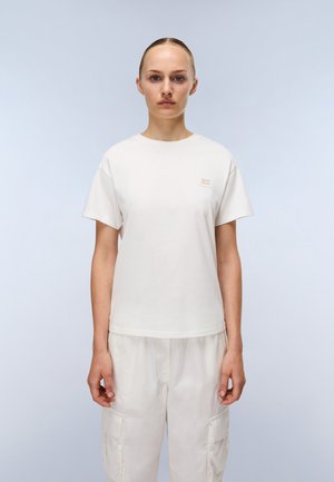 Witte t-shirt met korte mouwen van zachte katoen, voorzien van een ronde hals en subtiele branding op de linkerborst. Gecombineerd met lichte cargobroek.