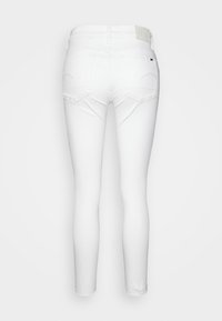 Pantalones vaqueros elásticos blancos con un corte ajustado, que cuentan con dos bolsillos traseros, una cinturilla suave y una etiqueta en la parte posterior por encima de la cinturilla.