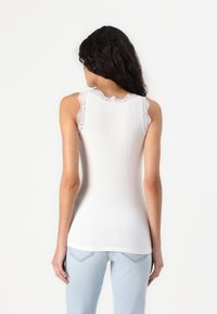 White tank top with lace trim on shoulders, ribbed texture, rounded neckline, and a fitted design, paired with light blue jeans.
