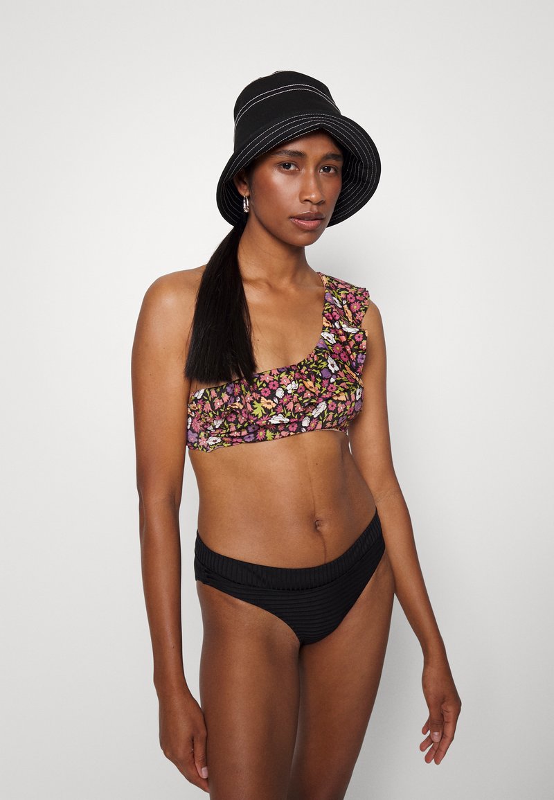 Top de bikini floral com detalhes em babados em tons de rosa, roxo e verde; combinado com calções pretos listrados sólidos. Chapéu bucket preto com listras brancas.