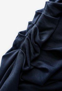 Tmavě modrá tkanina s jemnou strukturou, s mačkanými záhyby a hladkým povrchem, vystihující lehký a elastický design.