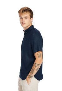 Camicia a maniche corte blu navy con bottoni, realizzata in tessuto leggero, con colletto, logo discreto sul petto e vestibilità comoda.