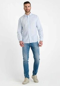 Lichtblauw gestreept overhemd met knopen, gecombineerd met vervaagde blauwe jeans en beige sneakers. Het overhemd heeft een klassieke kraag en lange mouwen.