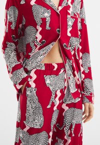 Červený pyžamový set s leopardím vzorem v černé a bílé barvě, s hladkým textilem, dlouhými rukávy a elastickým pasem na kalhotách.