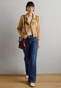Tan suede mootorrattajope, kreemjasüda ülikond, laiad sinised teksad ja valged kingad. Tume punane käekott minimalismiga disainiga. Puitpõrand taustana.