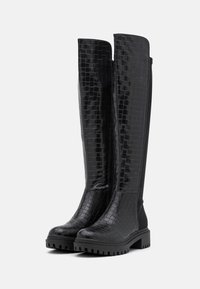 Botas negras hasta la rodilla con un acabado brillante y un diseño de piel de cocodrilo, que cuentan con una superficie texturizada y una suela de goma resistente.