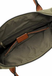 Intérieur en tissu vert olive d'un sac à main avec poche zippée, garniture en cuir marron et tirette de fermeture éclair sombre, présenté ouvert sur fond blanc.