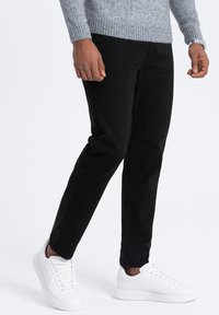 Pantalons en coton noirs avec une coupe slim, présentant une texture lisse et des coutures minimales, associés à des baskets blanches.