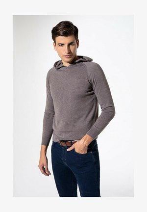 Hoodie gris en maille avec une poche avant, des poignets côtelés et une texture douce, associé à un jean bleu foncé et une ceinture marron.
