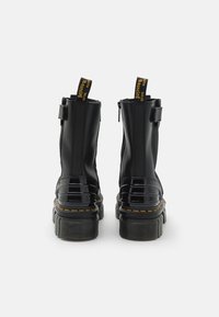Black ankle boots made of smooth leather with a glossy patent toe. Chunky platform sole with textured accents and yellow stitching detail.
