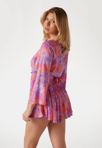Kukkakuosi mekko, jossa on elävä oranssi ja violetti paisley-kuvio, pitkät levenevät hihat, vartalon myötäinen vyötärö ja lennokas hame.