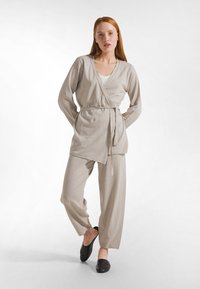 Světlý béžový zavinovací top s dlouhými rukávy a zavazováním v pase, doplněný volnými béžovými kalhotami. Jednoduchá, texturovaná látka s ležérním designem.