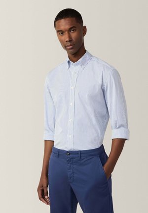 Blau-weißer gestreifter Button-up-Hemd mit Kragen, hochgekrempelten Ärmeln und glattem Stoff. Getragen mit navyblauen Hosen, die Taschen an den Seiten haben.