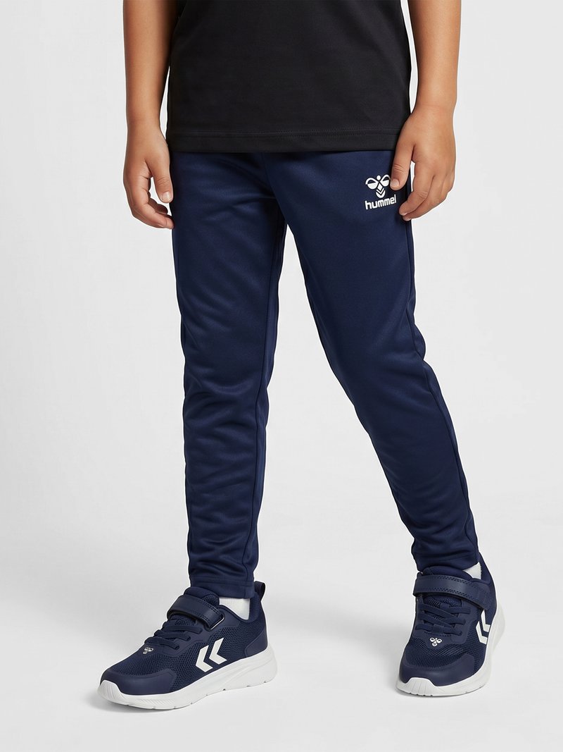 Child wearing navy blue hummel track pants and matching sneakers with white soles, standing against a plain light background.