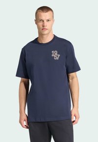 Marineblaues Baumwoll-T-Shirt mit kurzen Ärmeln und Rundhalsausschnitt, mit einem hellfarbenen "1957"-Motiv auf der linken Brustseite.