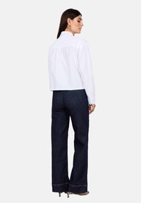 White cropped shirt with a high collar and gathered back detail, paired with dark blue denim wide-leg pants featuring visible stitching.
