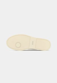Beige rubber shoe sole with textured grip, circular pattern near toe, rectangular pattern near heel, and "BOSS" logo in the center.