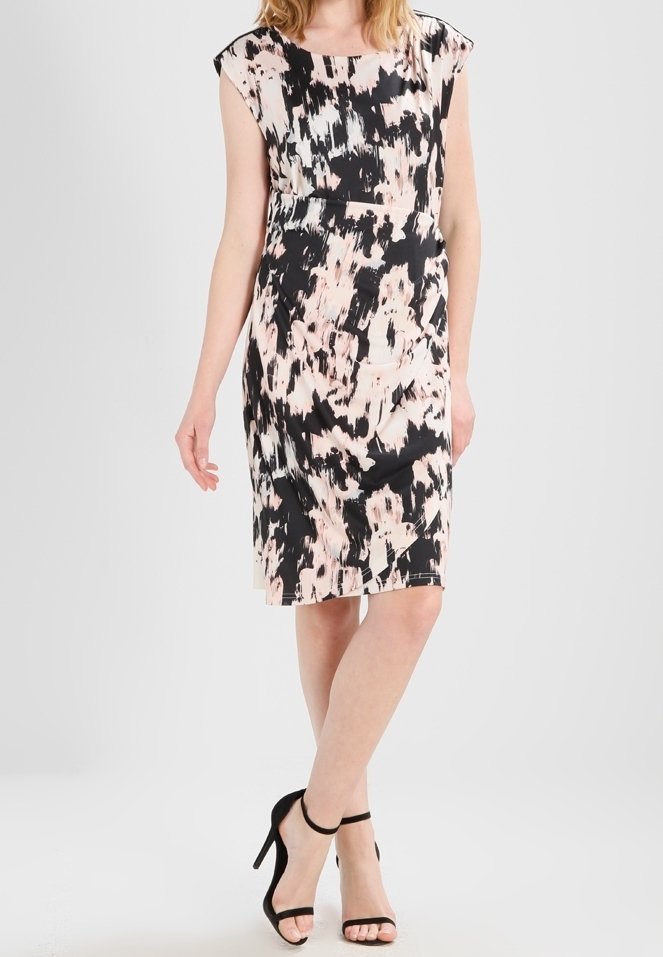 Femme portant une robe sans manches longueur genoux avec un imprimé abstrait noir et beige, associée à des escarpins noirs à bride cheville.