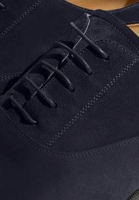 Scarpe stringate in suede blu navy con una texture liscia, cuciture dettagliate e un design a punta arrotondata. Gli occhielli sono rinforzati per una maggiore durabilità.